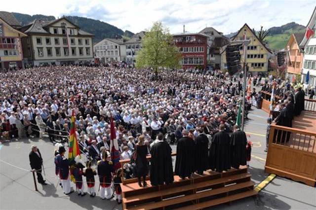 Die Stimmbürgerinnen und Stimmbürger haben sich auf dem Landsgemeindeplatz mitten in Appenzell versammelt. Vor ihnen ist die Tribüne mit dem Regierungsrat und eine zweite Tribüne mit den Ehrengästen.