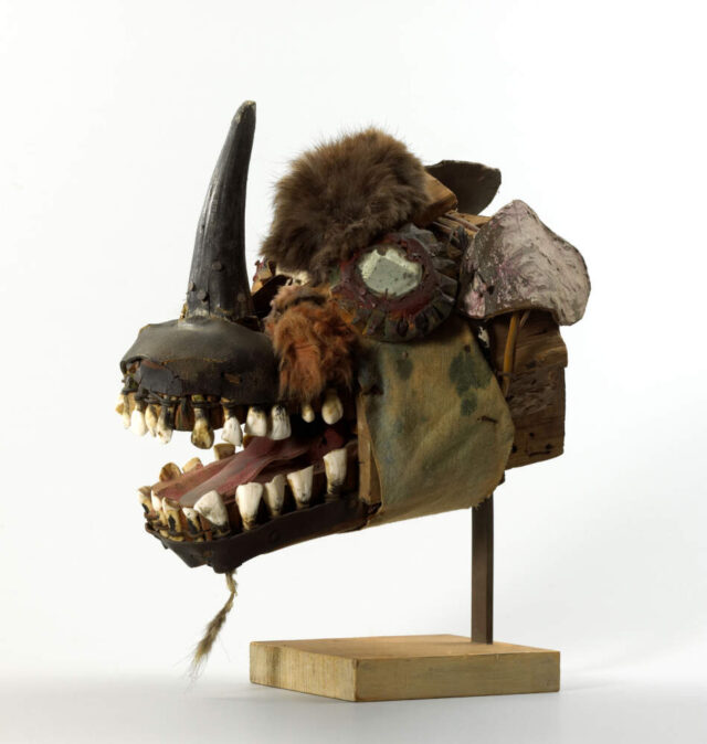 Eine Skulptur von einem Fantasiekopf mit einem Horn auf der Nase und mit offenen Mund, in dem man die Zähne sieht.