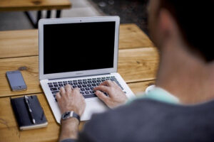 Ein Mann sitzt an einem Holztisch und arbeitet am Computer.