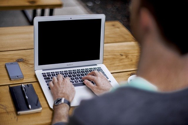 Ein Mann sitzt am Tisch. Er schreibt auf einem kleinen Computer.