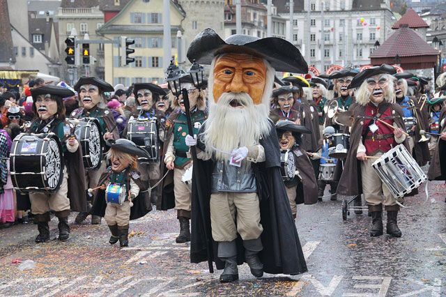 Fasnachtsumzug: Die Gruppe tr&auml;gt &uuml;bergrosse K&ouml;pfe aus Pappmache. Sie spielen verschiedene Trommeln.