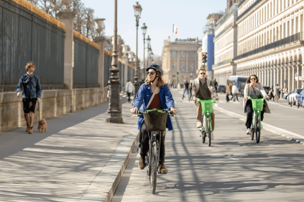 Auf einer Pariser Strasse fahren zwei Velofahrerinnen und ein Velofahrer.