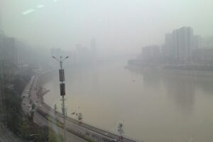 Ein breiter Fluss fliesst durch eine Stadt. Smog verhüllt die Gebäude am Ufer.