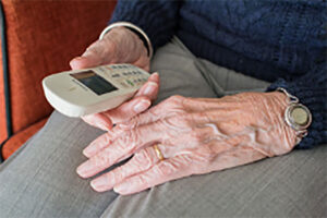Eine ältere Frau hält ein weisses Telefon in der rechten Hand.