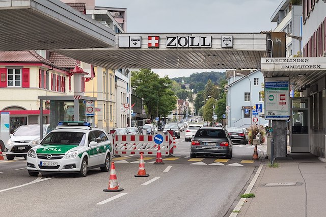 Ein Auto fährt über den Zoll. Der Übergang ist mit einem Dach bedeckt. Am Dach steht auf einem Schild Zoll. Links davon ist das Schweizer Wappen.